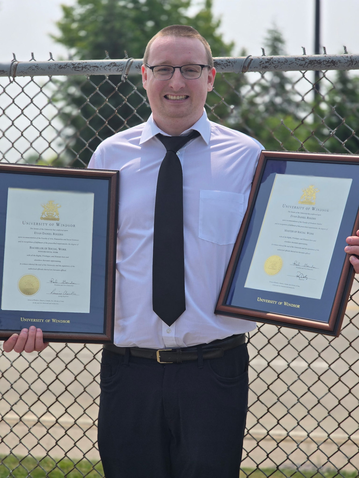 Evan Rogers holding framed Bachelor and Master of Social Work diplomas